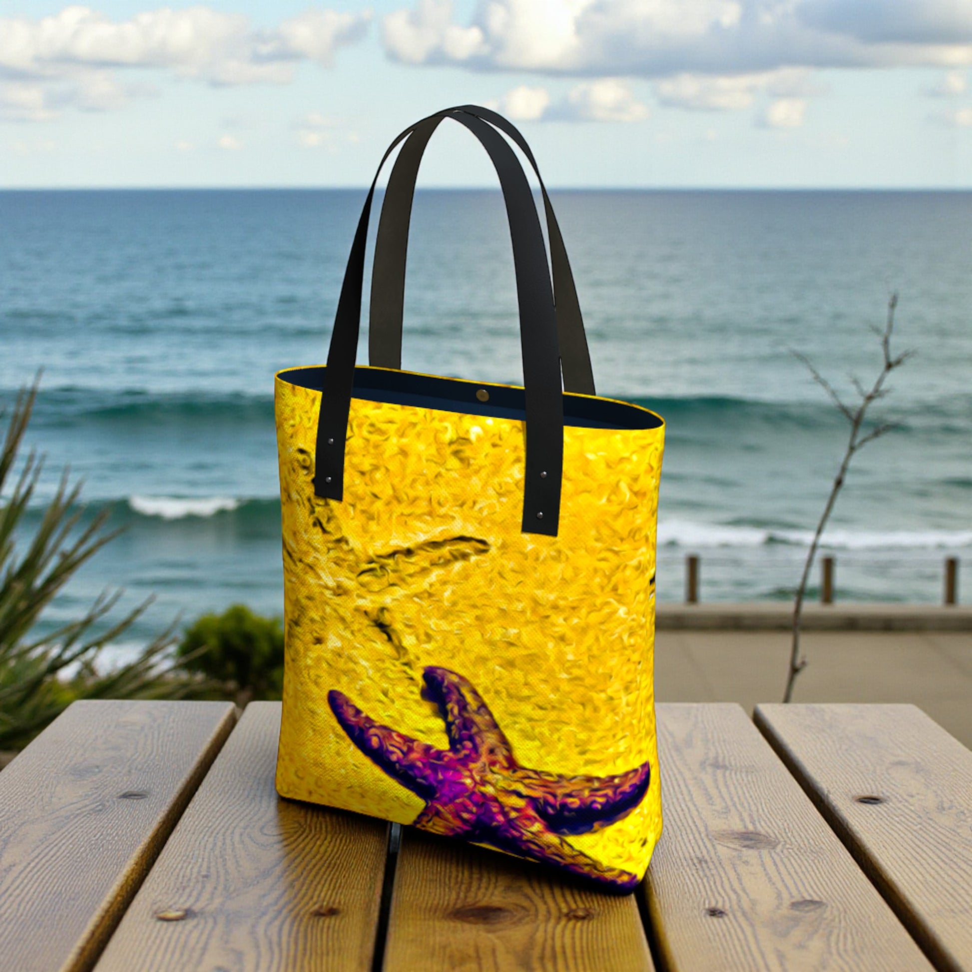 Yellow tote bag with a starfish design on a wooden table by the ocean.