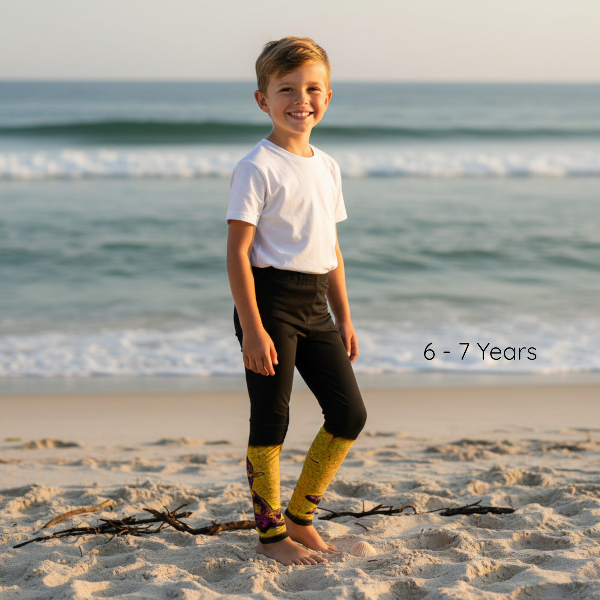 Child standing on a beach with ocean waves in the background, wearing a white shirt, black pants, and yellow socks.