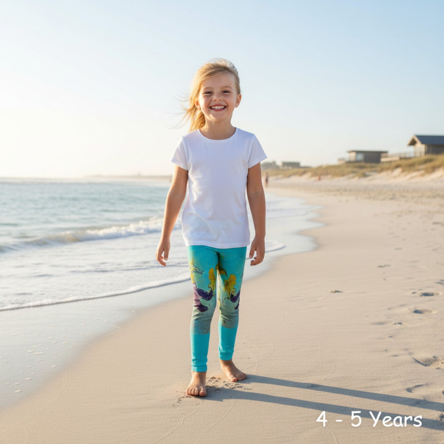 Young girl in colorful leggings and white shirt standing on a sandy beach.