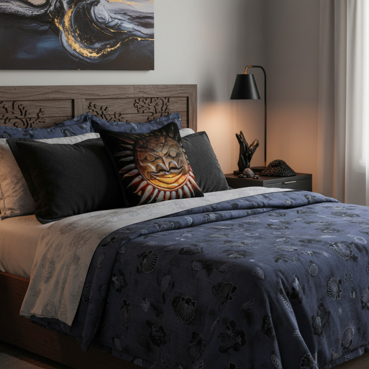 A styled bed in a bedroom featuring a dark blue patterned duvet cover, matching pillows, a black accent pillow with a sun design, and a gray headboard. A black floor lamp stands on a nightstand beside the bed.