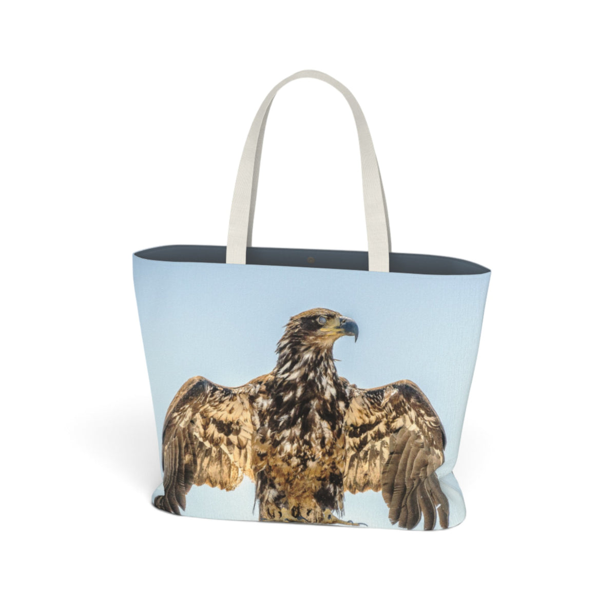 A tote bag with a large printed image of a golden eagle on the front, featuring light beige handles and a dark navy blue interior, shown against a plain white background.