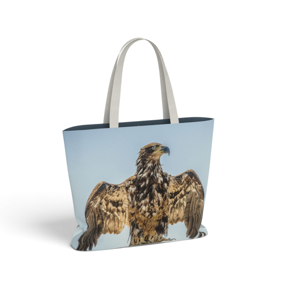 A tote bag with a large printed image of a golden eagle on a light blue background, featuring light gray fabric shoulder straps, shown on a clean white background.