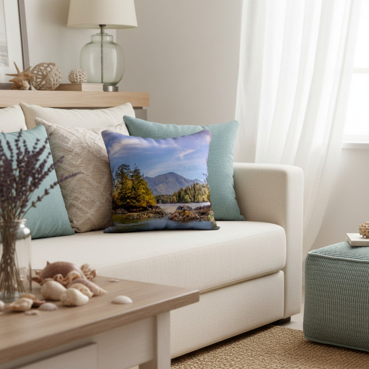 A square throw pillow featuring a scenic mountain lake landscape print, styled on a cream-colored sofa in a bright, modern living room.