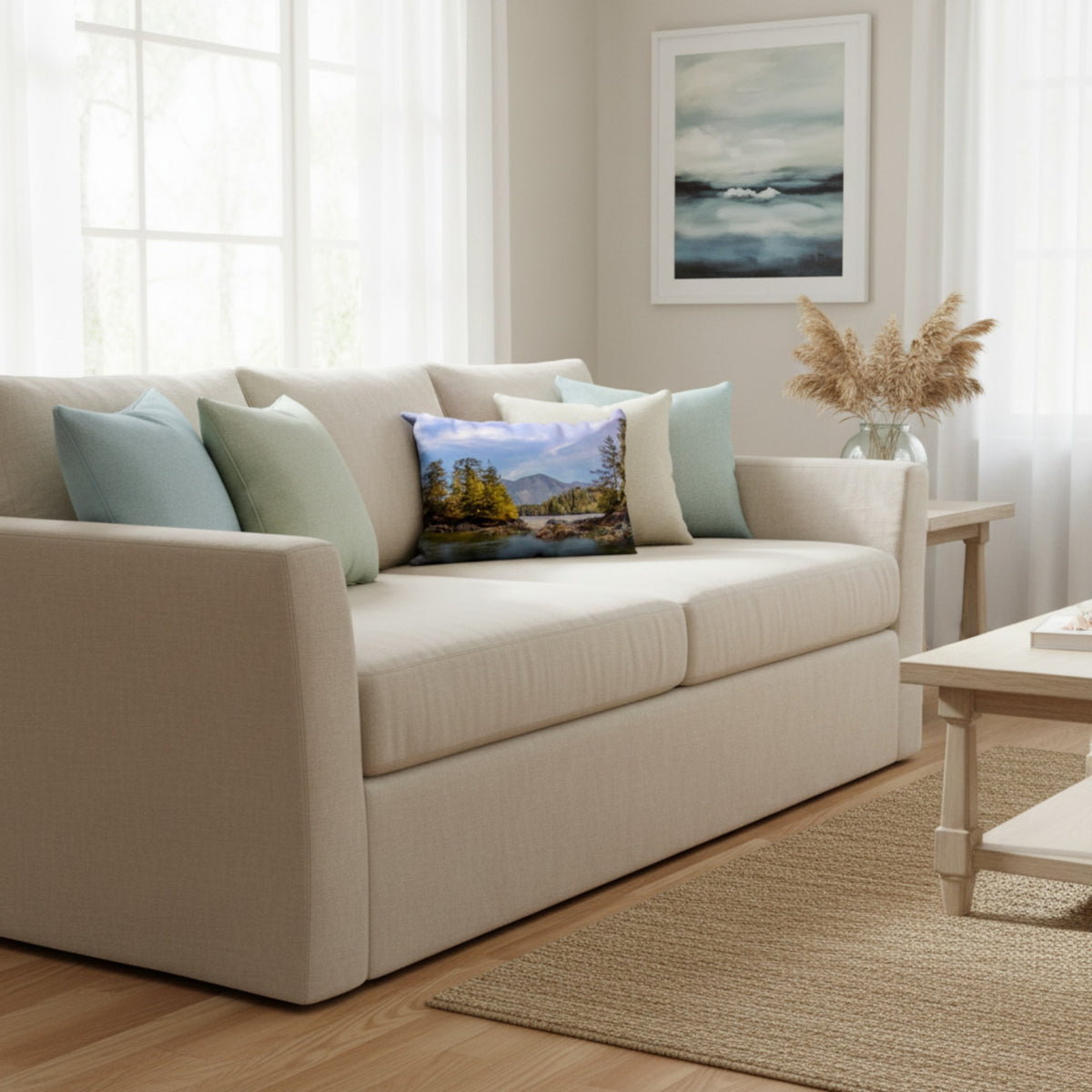 A beige upholstered loveseat in a bright, modern living room, styled with light blue and sage green throw pillows and a central landscape print pillow.