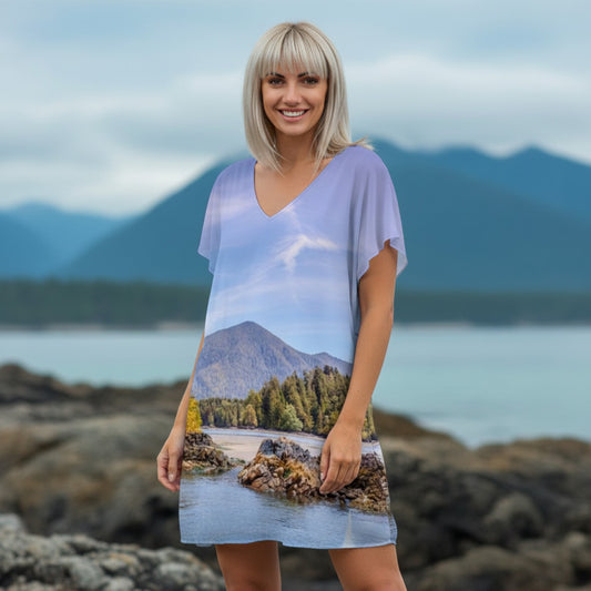 Woman wearing a dress with a nature print standing on rocks with mountains and water in the background