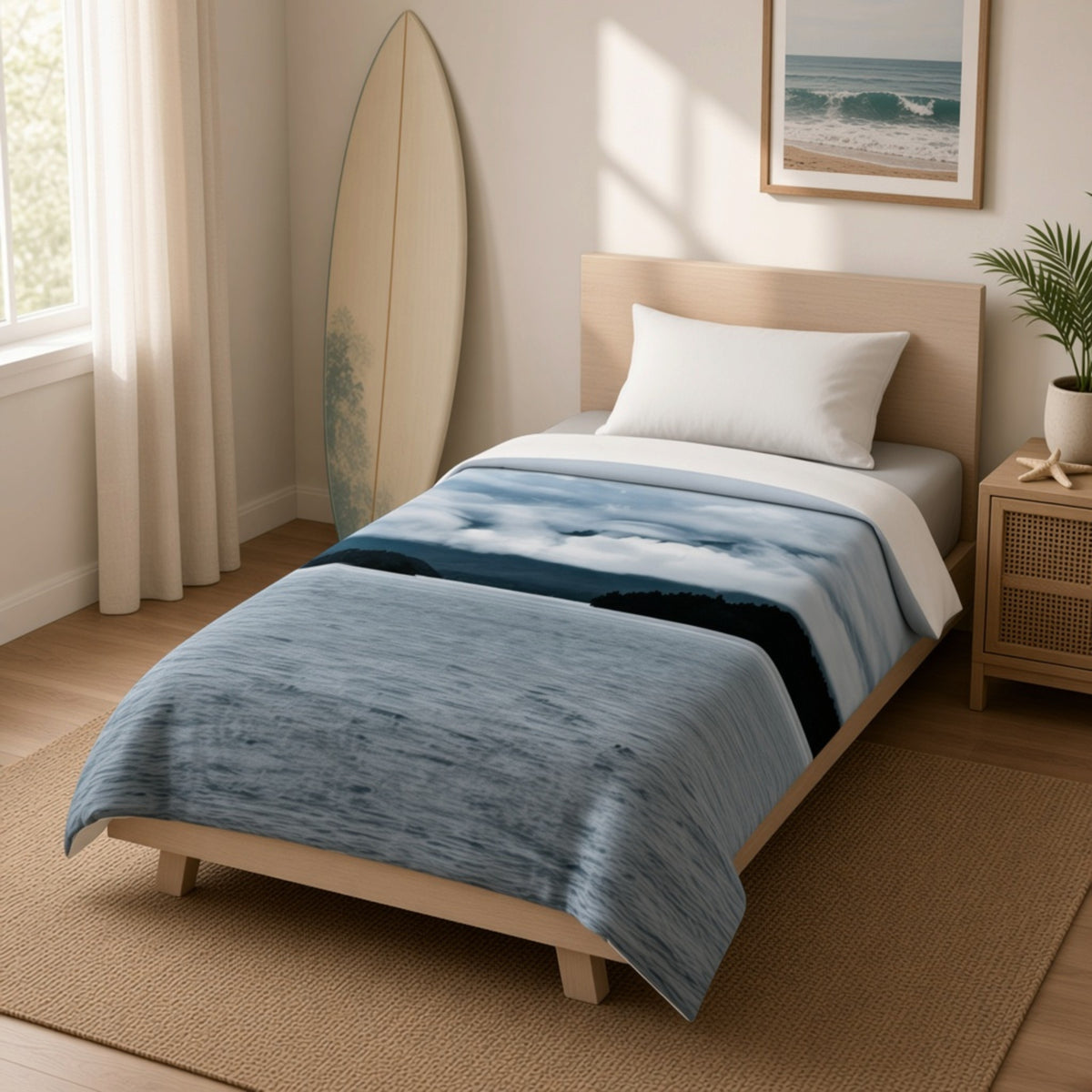 A single bed in a bright, modern bedroom setting, styled with a blue and white abstract print blanket, white pillow, and light wood headboard. A tall surfboard leans against the wall, and a small potted plant sits on the wooden nightstand.