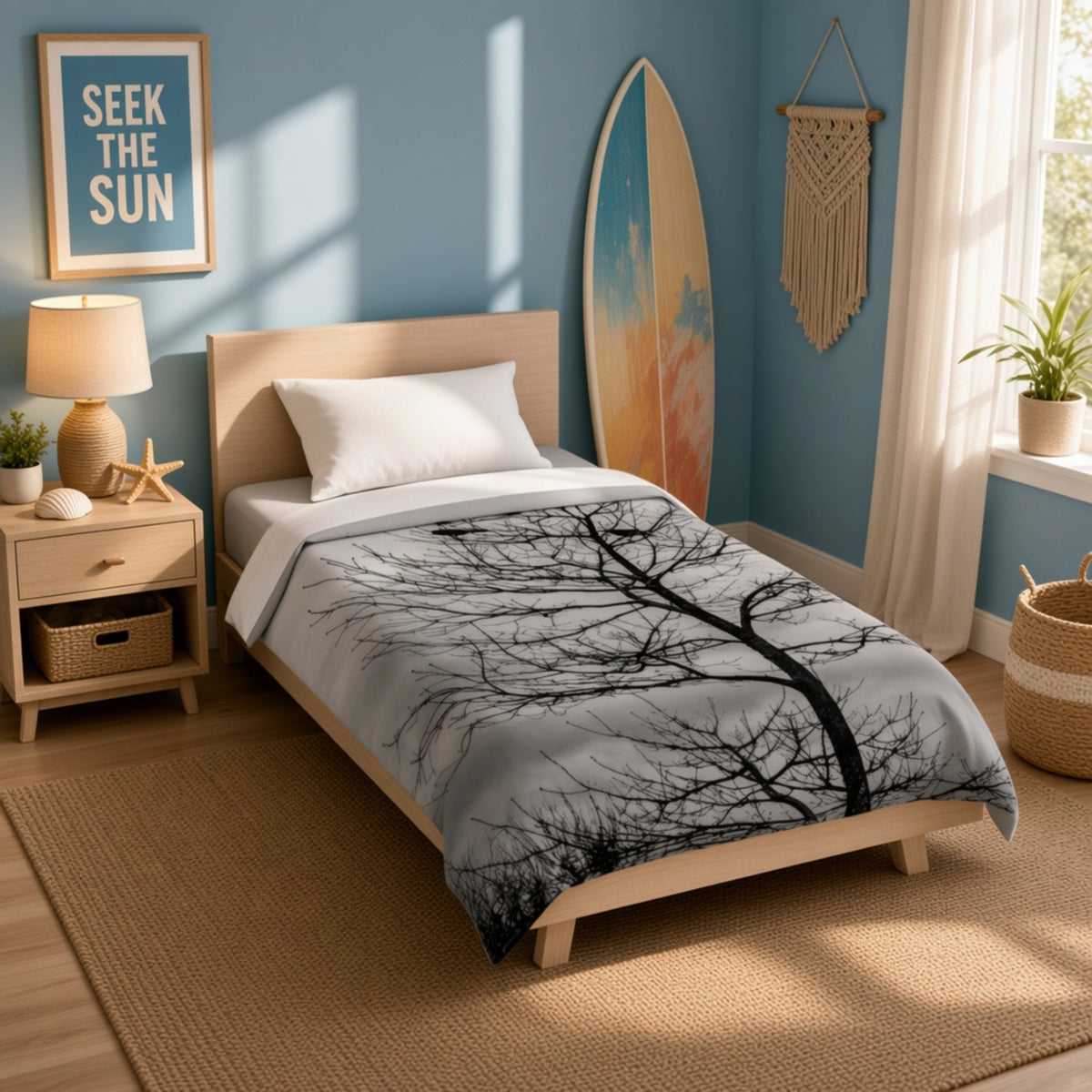 A single bed in a styled bedroom setting, featuring a light gray comforter with a black tree branch pattern. The room has blue walls, a wooden nightstand, a lamp, a surfboard leaning against the wall, and a window with white curtains.