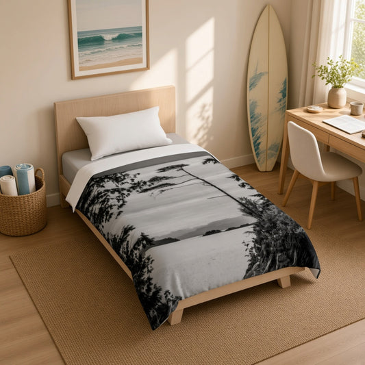 A bed dressed in a black-and-white landscape print duvet cover with white pillows and a cream throw blanket, styled in a bright bedroom with a wooden headboard, side table, curtains, and a straw hat.