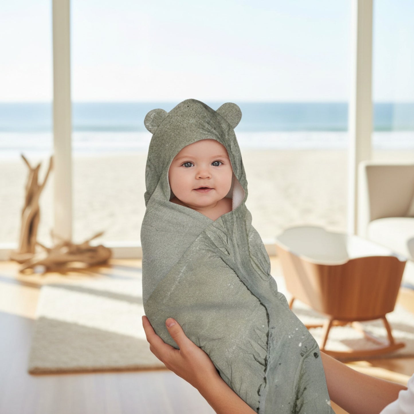 Baby wrapped in a green hooded towel with a bear design, sitting in a bright room.