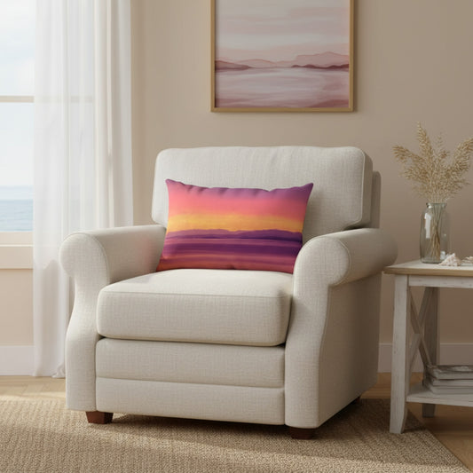 A cream-colored upholstered armchair in a bright living room setting, featuring a square throw pillow with a colorful sunset gradient pattern in pink, orange, yellow, and purple.