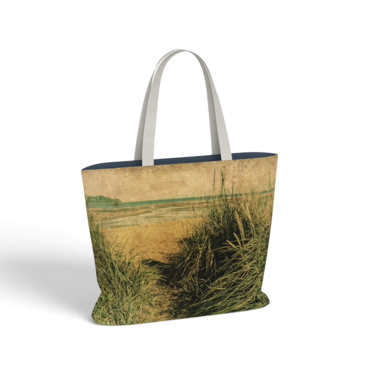 A tote bag featuring a textured, vintage-style print of beach grasses and dunes in earthy green and tan tones, with contrasting light gray shoulder straps, shown on a white background.