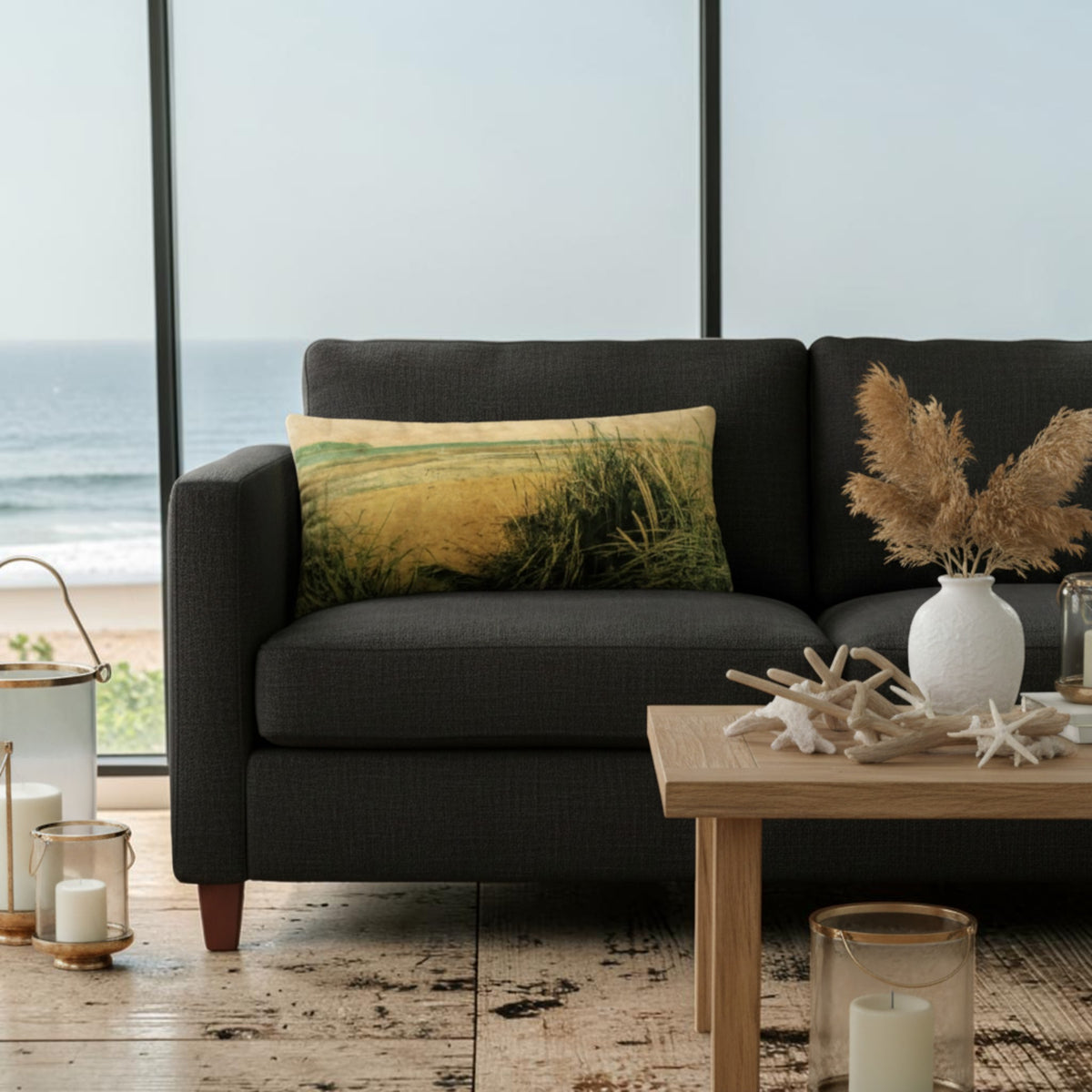 A dark charcoal gray fabric sofa in a coastal living room setting, featuring a square throw pillow with a beach grass print and a light wood coffee table in the foreground.