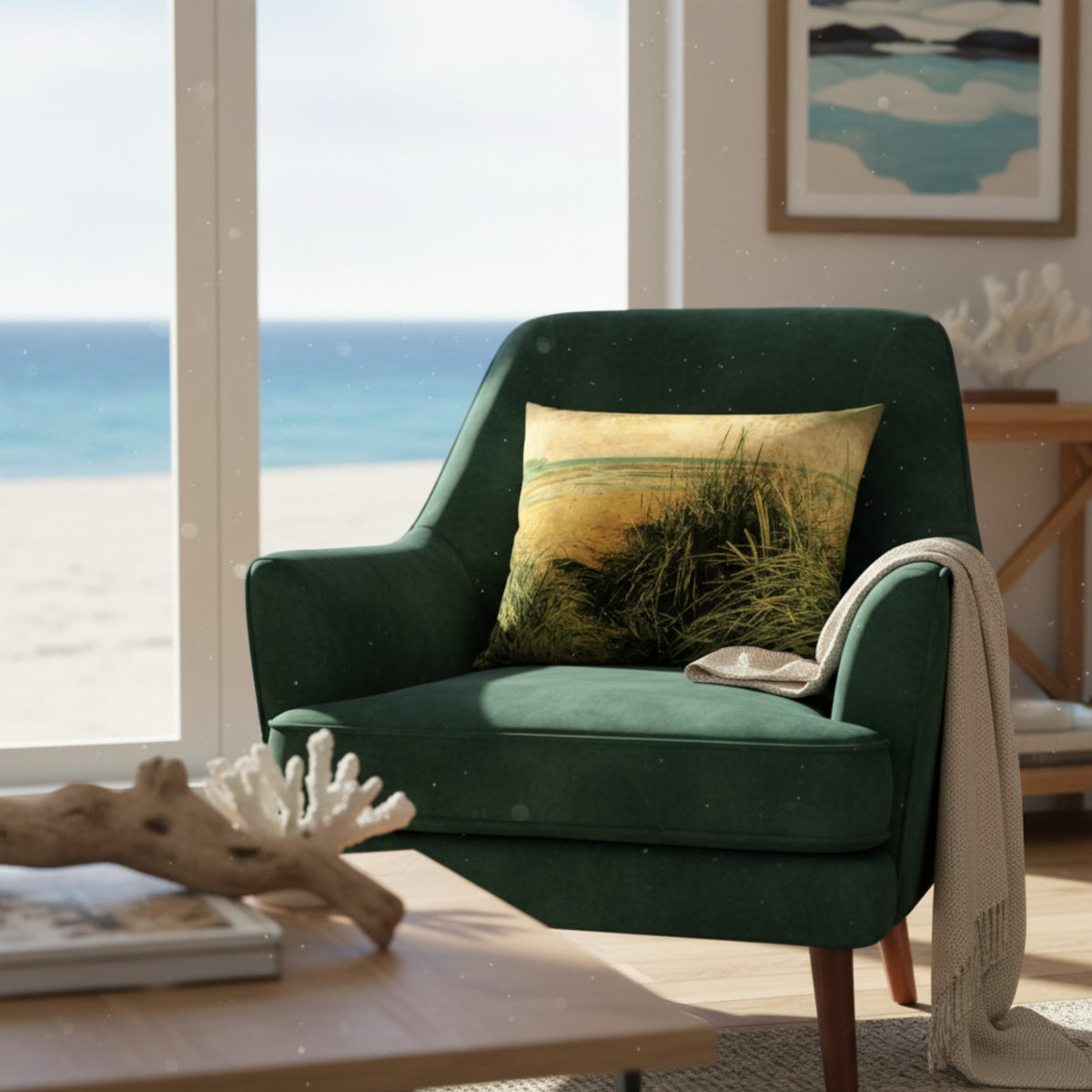 A dark green velvet armchair in a bright beach-view room, styled with a square beach-print throw pillow and a cream knit throw blanket draped over the arm.