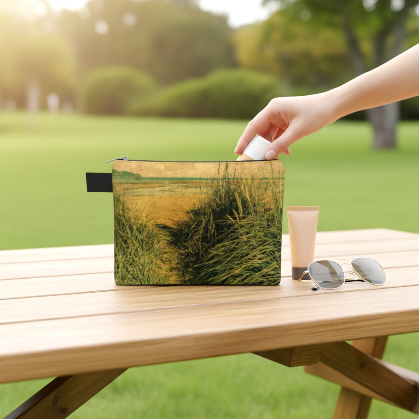 Hand reaching for a pouch with a grassy field design on a wooden table outdoors.