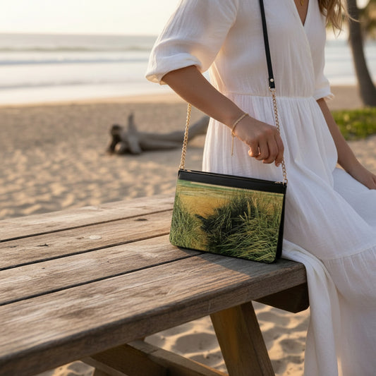 Woman in a white dress holding a green and black handbag on a wooden bench by the beach.