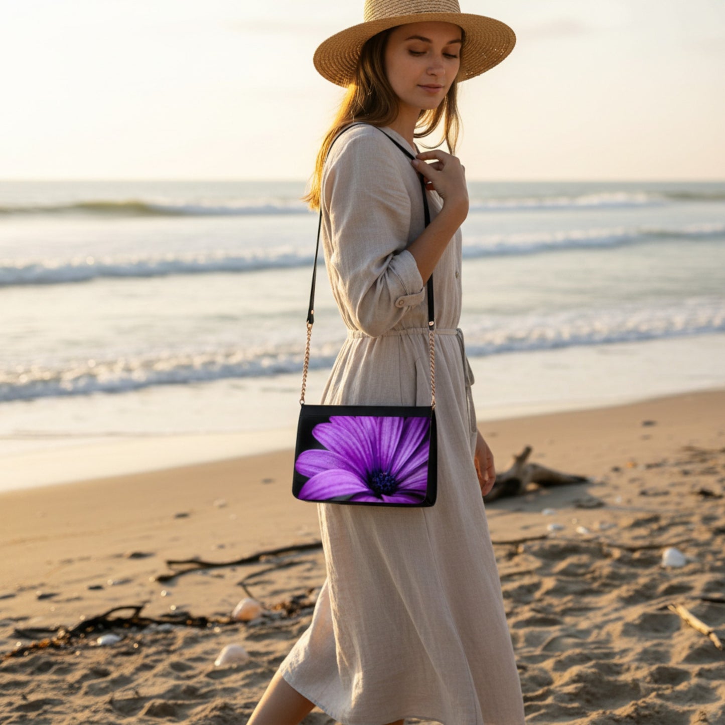 Woman on a beach holding a black crossbody bag with a purple flower design.