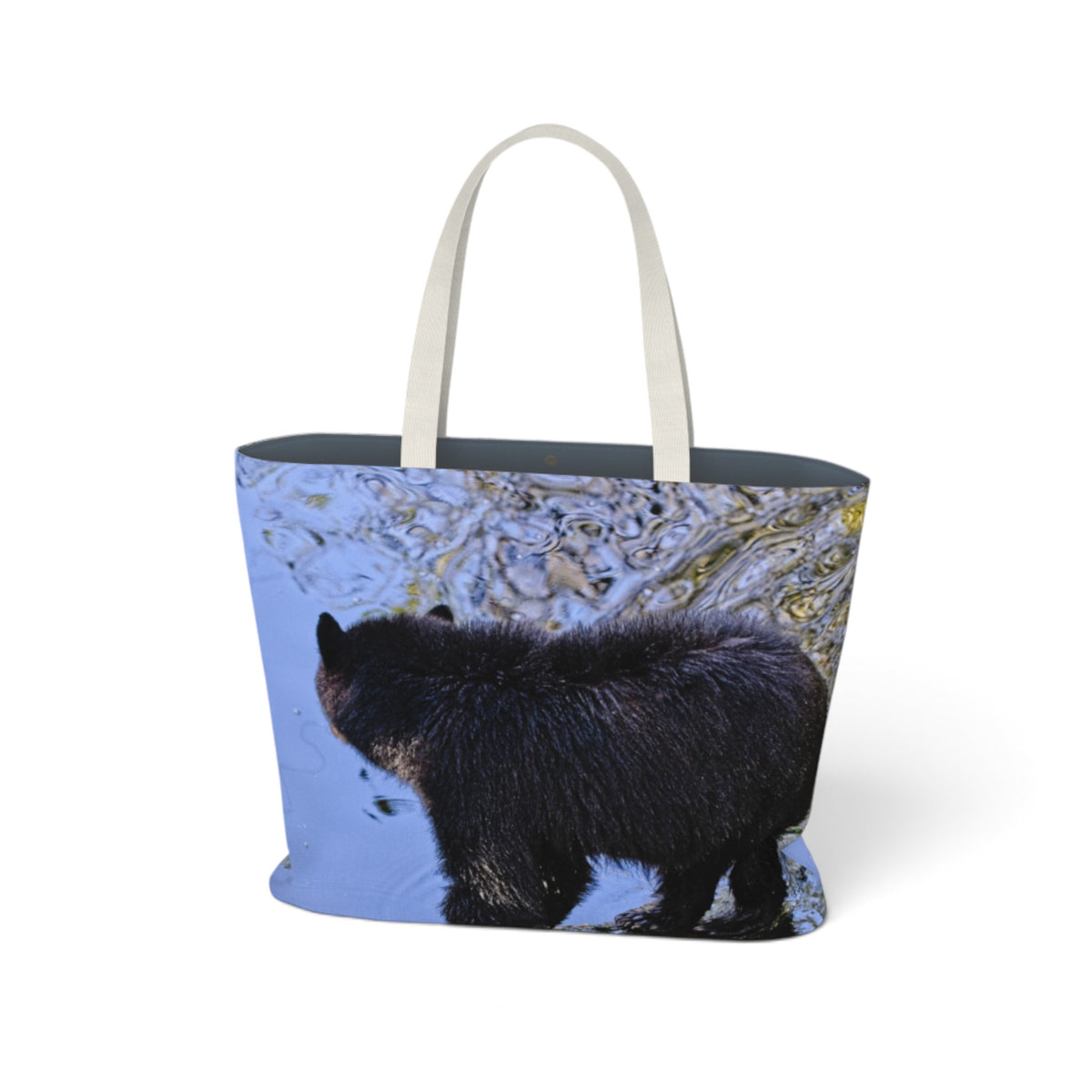 A tote bag with a photographic print of a black bear walking through rippling water, featuring light beige fabric handles and a dark gray interior lining, shown on a plain white background.