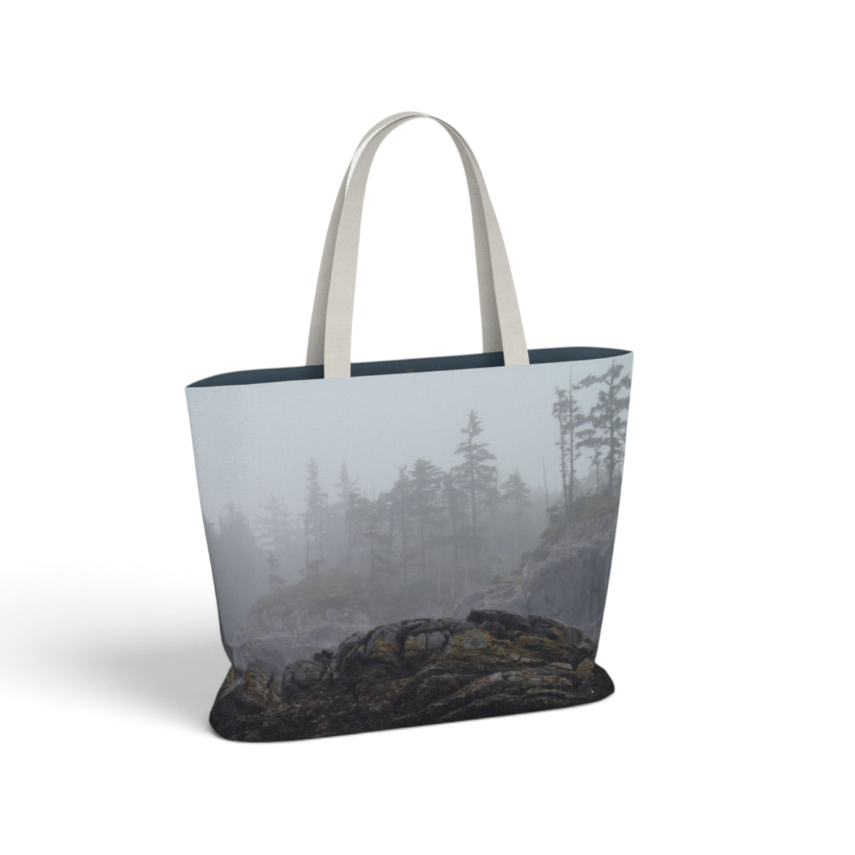 A tote bag featuring a photographic print of a misty pine forest and rocky shoreline, with light beige shoulder straps, shown on a plain white background.