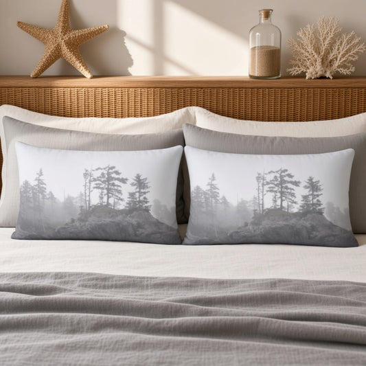 Two rectangular throw pillows with a gray and white misty forest print, styled on a bed with neutral linens and a wicker headboard in a warm, sunlit room.