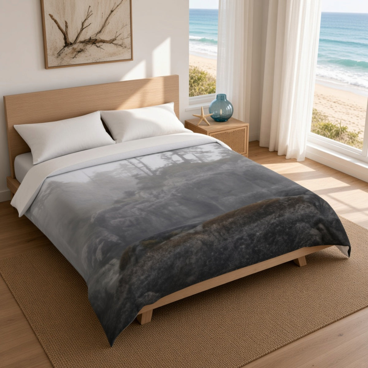 A bed dressed in a gray and black misty forest print comforter with white pillows, styled in a bright bedroom with a beach view through large windows.