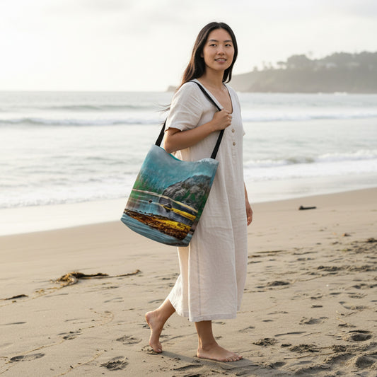 Woman holding a beach bag with a scenic design on a sandy beach.