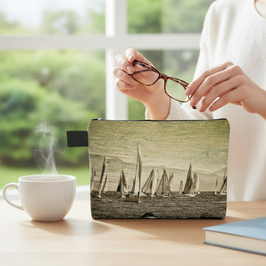 Person holding glasses above a pouch with sailboat design, next to a steaming cup of coffee on a table.