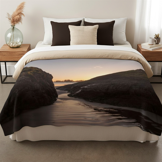 Van Isle Goddess Distant Sunset Tofino Coastal Blanket, soft polyester minky fabric, features a beach sunset scene with rocks and water.