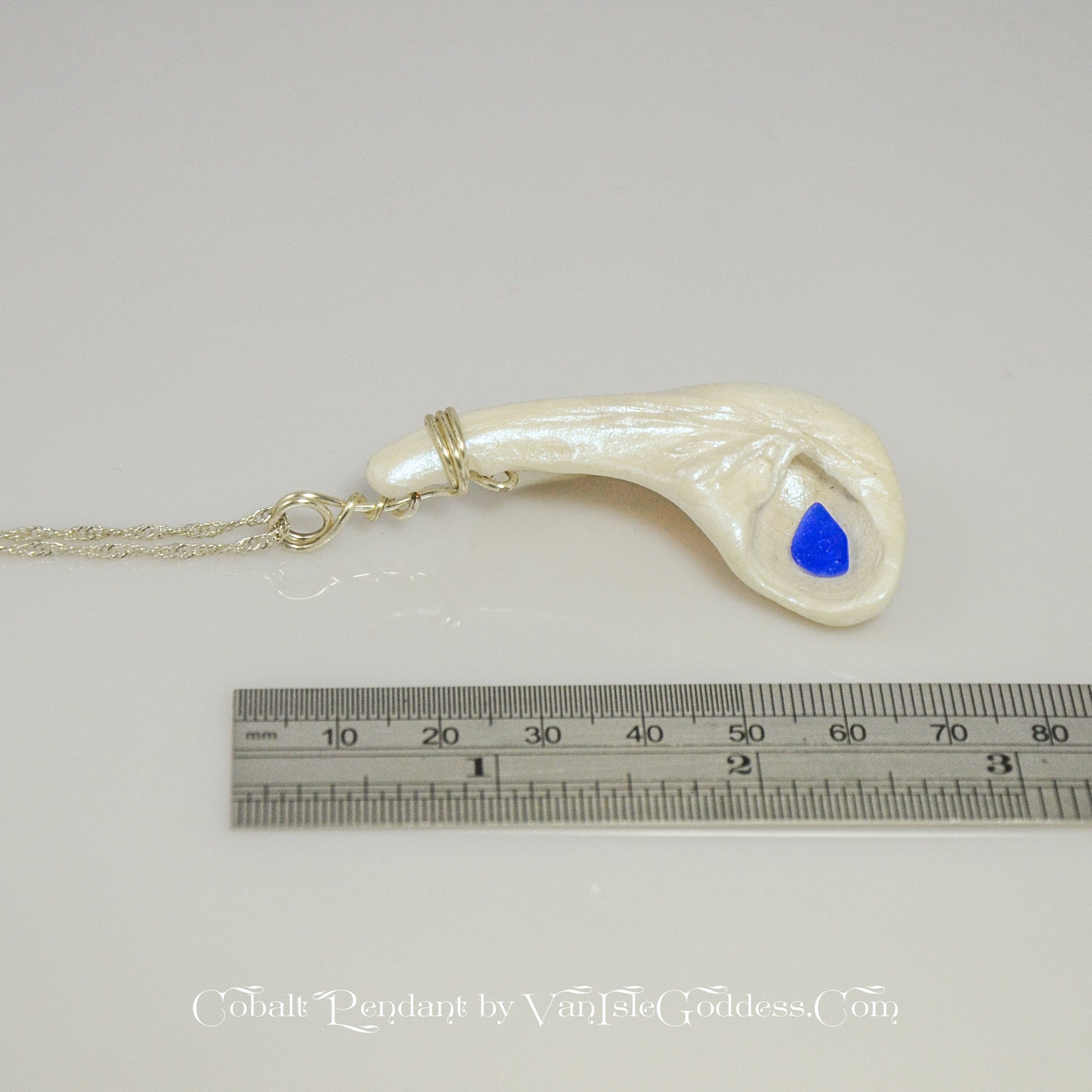 The cobalt pendant is shown on its side along a ruler so the viewer can see the length of the pendant.