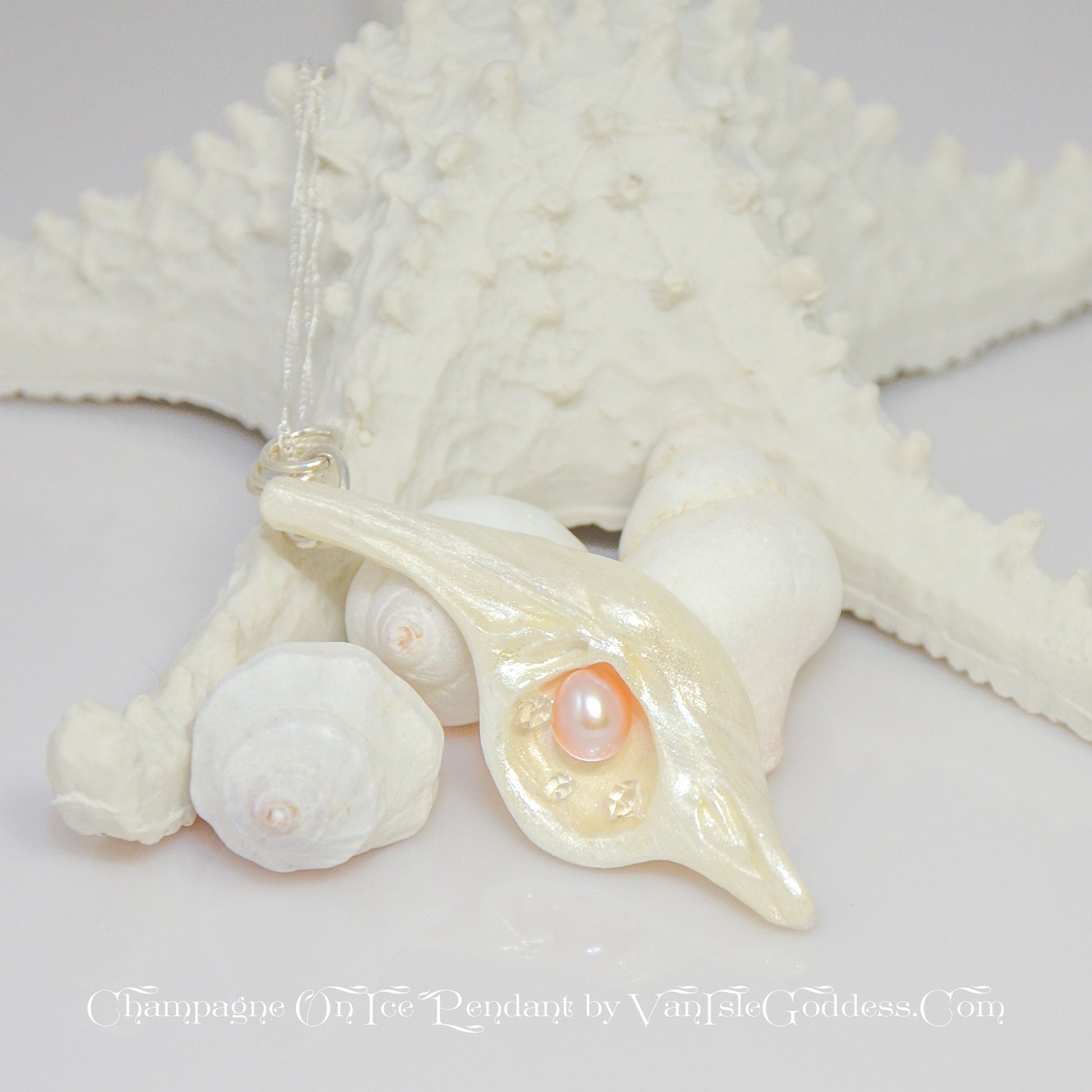 The pendant Champagne on Ice by Van Isle Goddess dot com is shown propped up against a few shells and a starfish.  