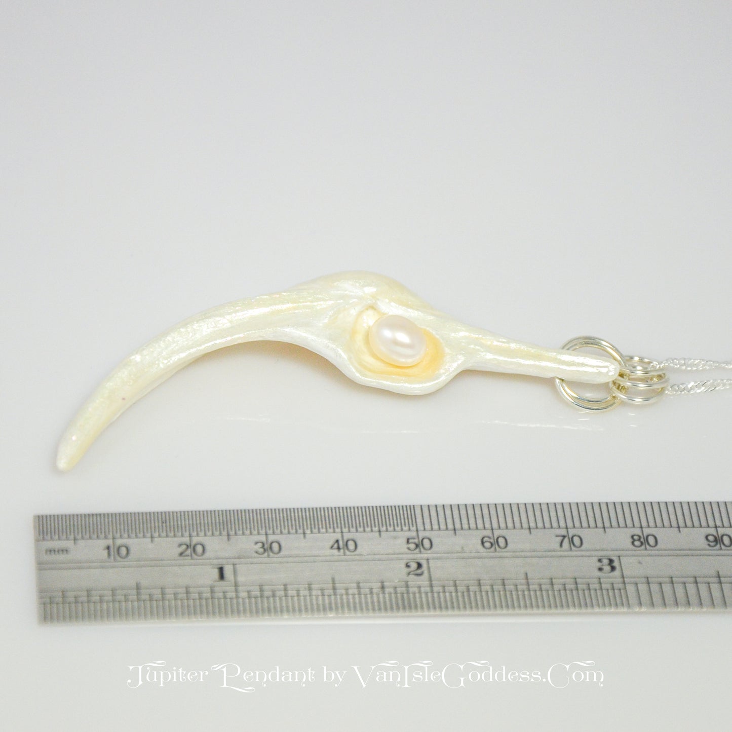 Jupiter is a natural seashell pendant with a real freshwater pearl. The pendant is shown laying on its side so the viewer can see the length. of the pendant.