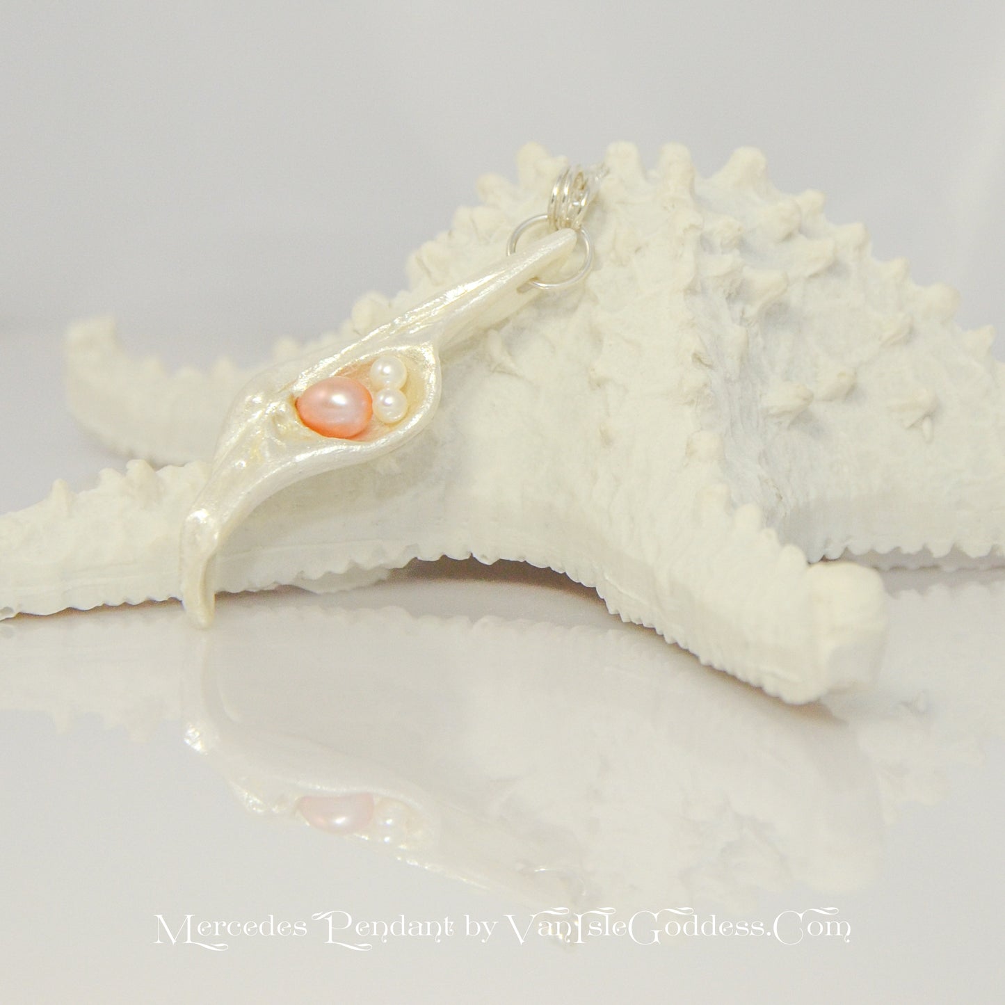 This natural seashell pendant has a real 7-8mm pink freshwater pearl and two baby pearls. The pendant is shown resting a a starfish.  The words printed on the bottom read: Mercedes Pendant by Van Isle Goddess dot com
