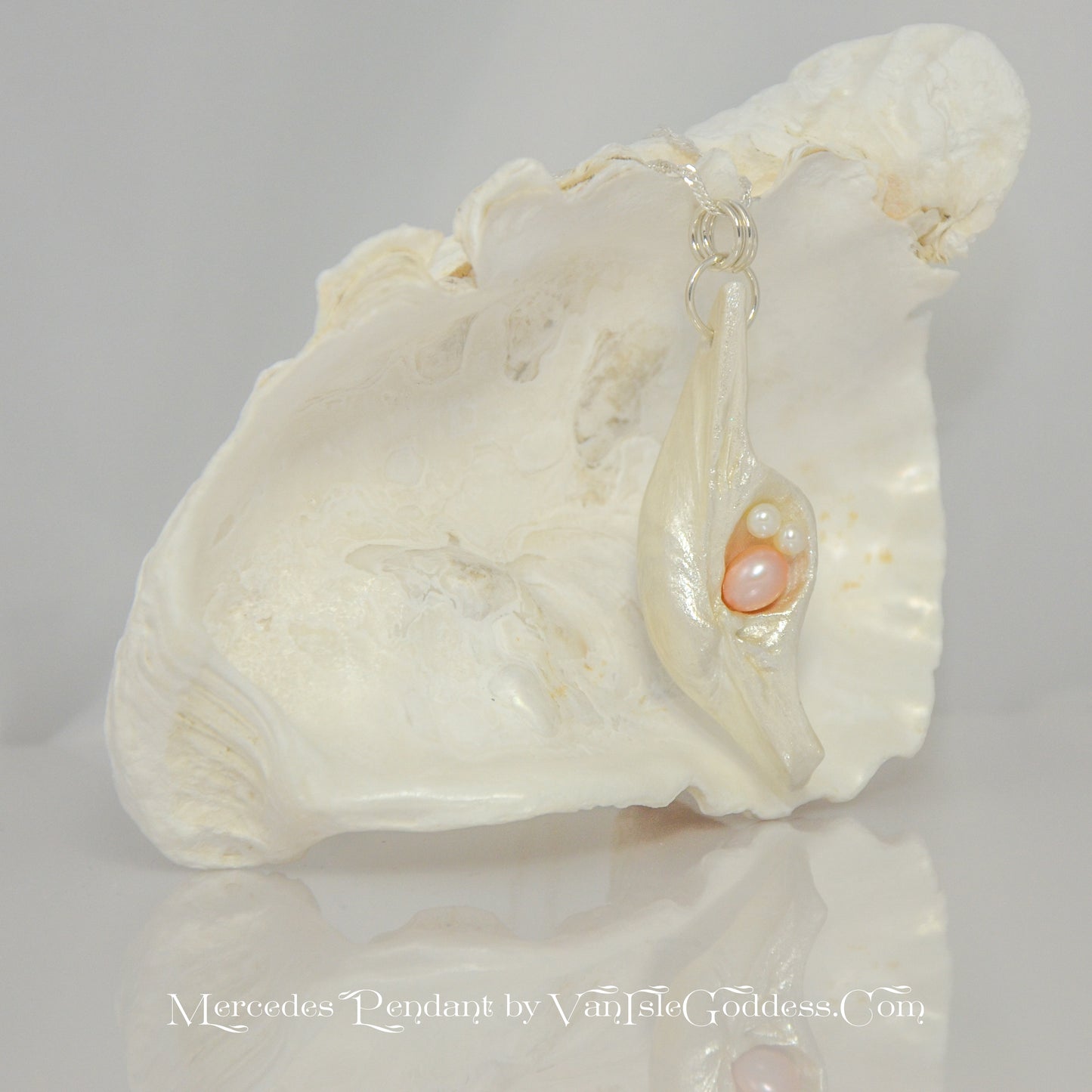 This natural seashell pendant has a real 7-8mm pink freshwater pearl and two baby pearls. The pendant is shown in front of a larger seashell.  The words on the bottom of the image read: Mercedes Pendant by Van Isle Goddess dot com