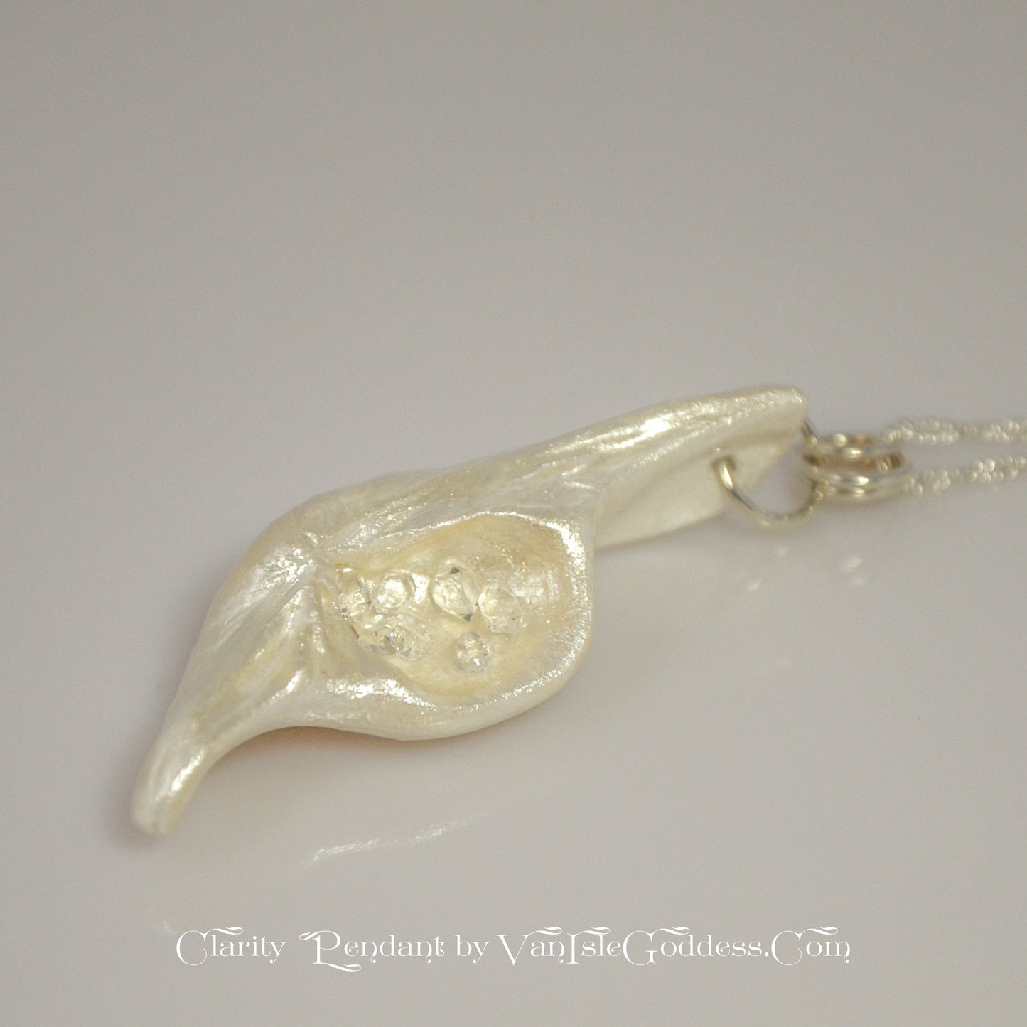 Beautiful pendant called Clarity.  Clarity is a natural seashell from the beach of Vancouver island.with seven herkimer diamonds. The pendant is shown on its side at an agle to show the shape of the pendant.  The print on the bottom of the image says Clarity Pendant by Van Isle Goddess dot com