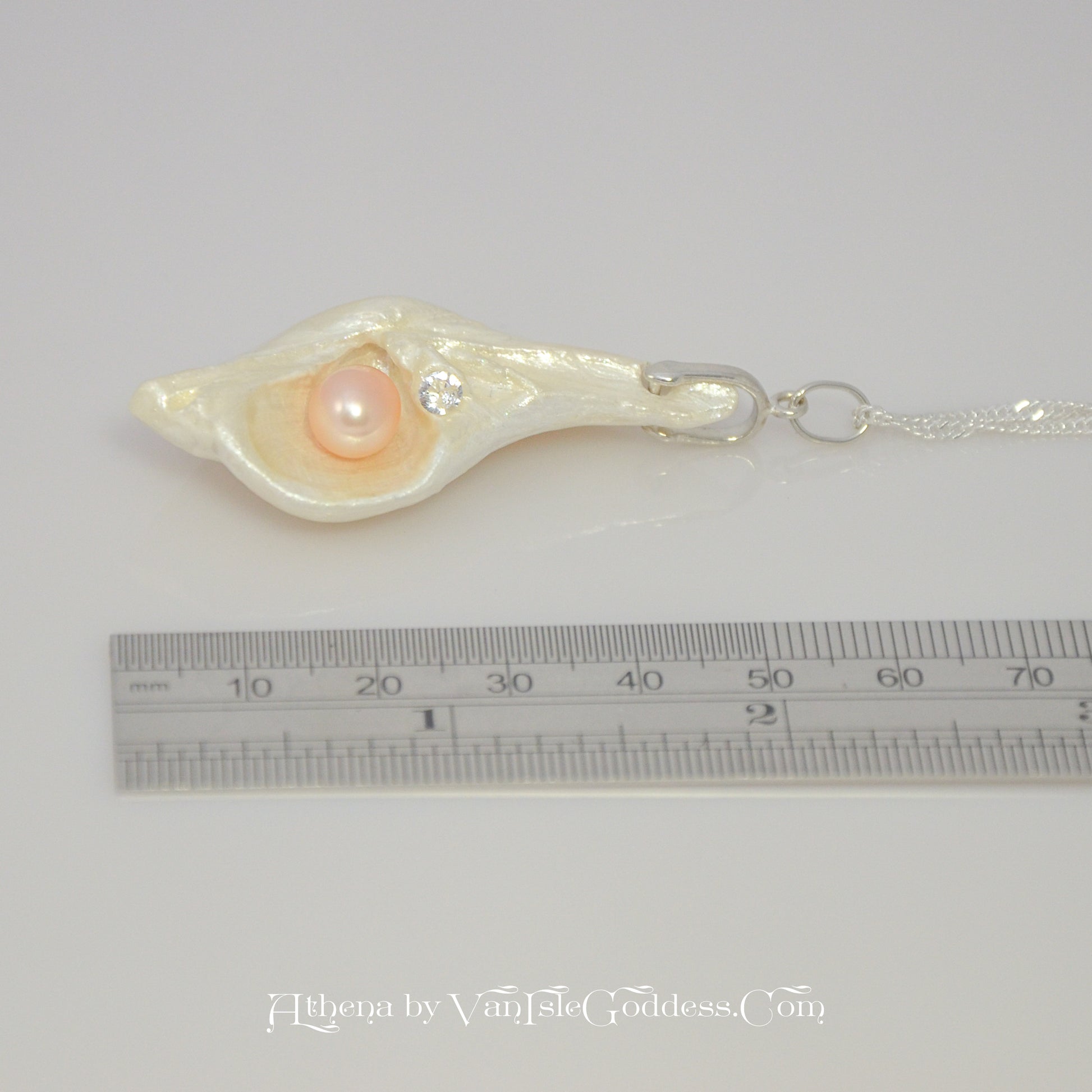 The pendant is laying on it side along a ruler so the viewer can see the length of the pendant.