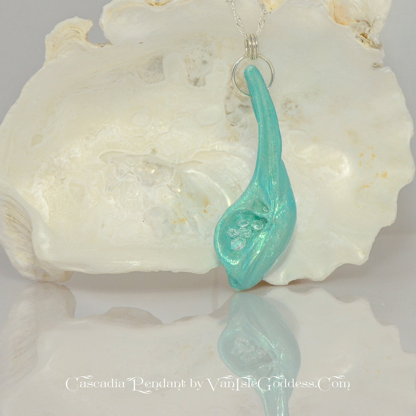 The Cascadia Pendant created with a natural seashell from the beaches of Vancouver Island.  The seashell is turquoise and has high quality herkimer diamonds. The pendant is hanging from a larger seashell.  The print on the bottom of the image says: Cascadia Pendant by Van Isle Goddess dot com