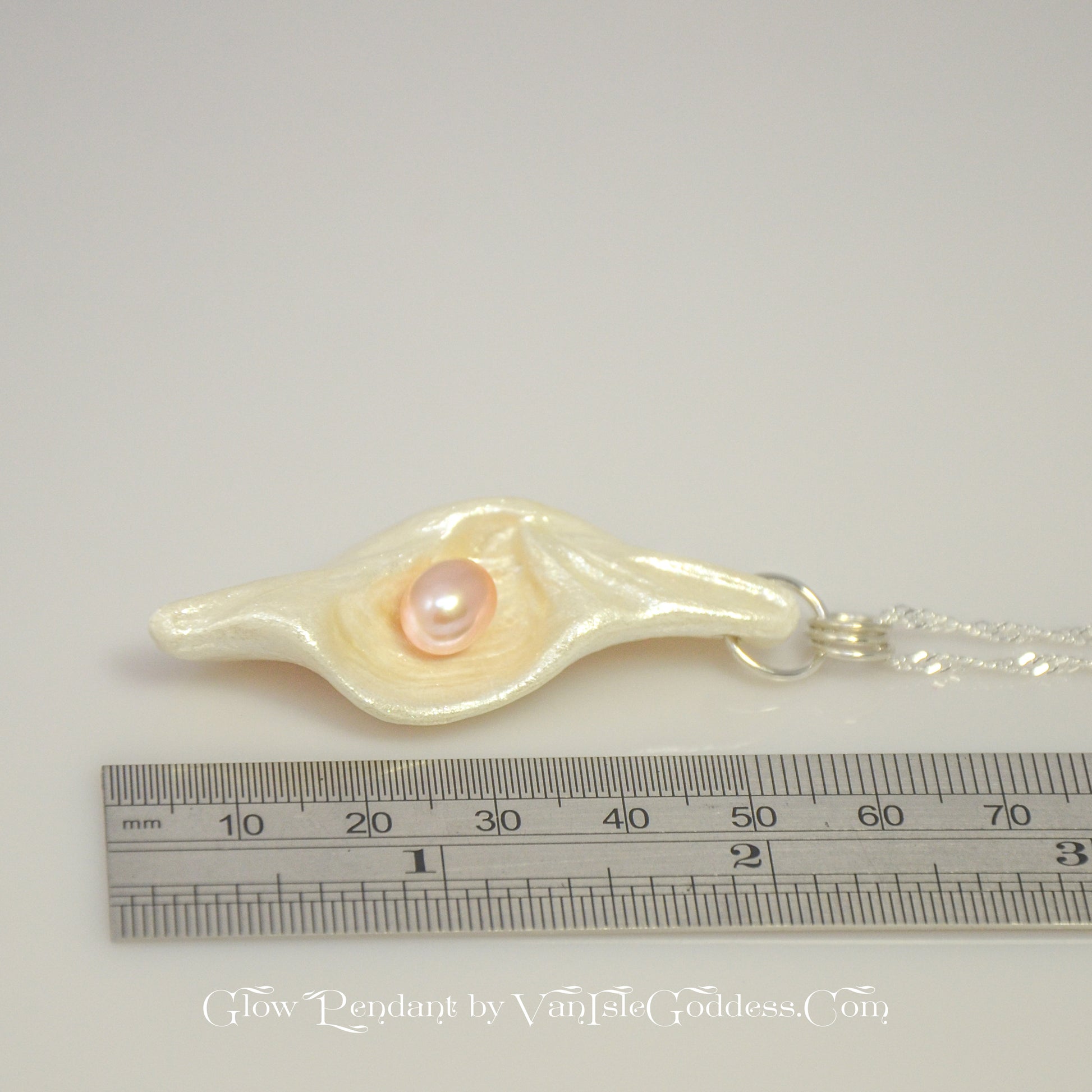 Glow natural seashell pendant with a pink freshwater pearl. The pendant is laying along a ruler so the viewer can see the length of the pendant.