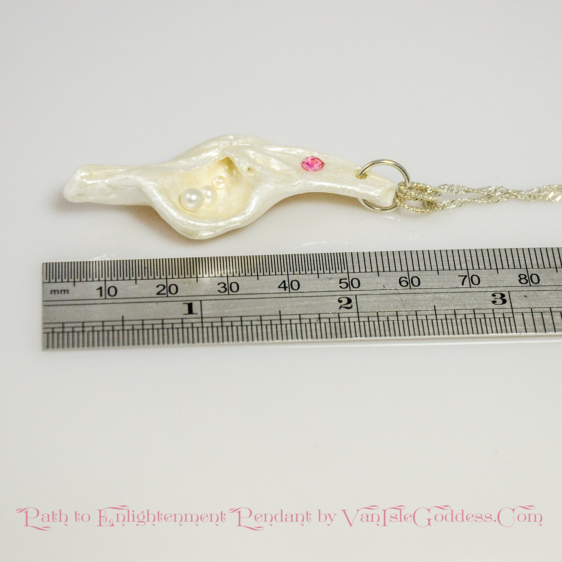 A trio of white baby freshwater pearls and a teardrop rose cut pink tourmaline gemstone compliments the seashell pendant beautifully. The pendant is shown laying down along a ruler so the viewer can see the length of the pendant.