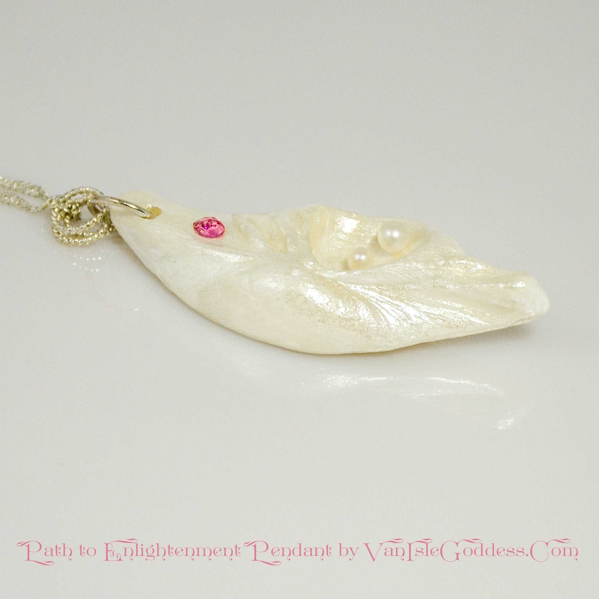 A trio of white baby freshwater pearls and a teardrop rose cut pink tourmaline gemstone compliments the seashell pendant beautifully. The pendant is shown laying down on a white table top.