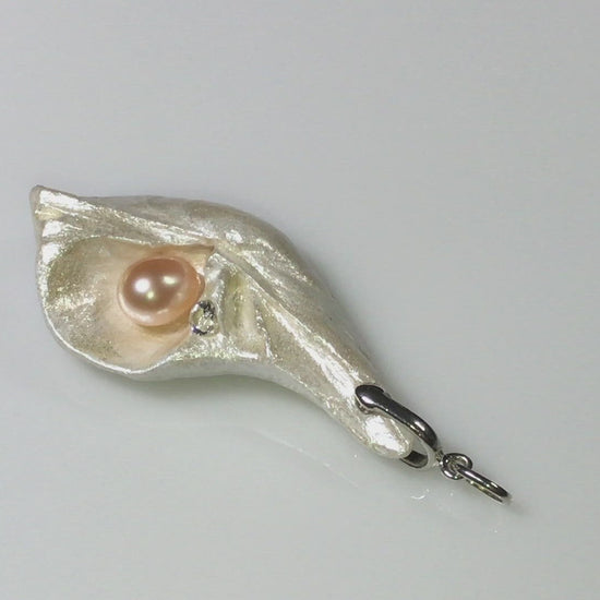 Athena is the name of the pendant being showcased.  It is a natural seashell from the beaches of Vancouver Island. The pendant has a real pink freshwater pearl and a faceted herkimer diamond. It is being showcased in the video.