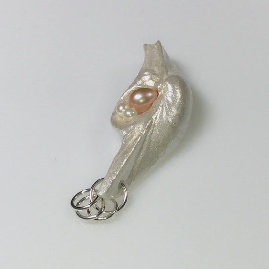 A video showcasing This natural seashell pendant has a real 7-8mm pink freshwater pearl and two baby pearls.