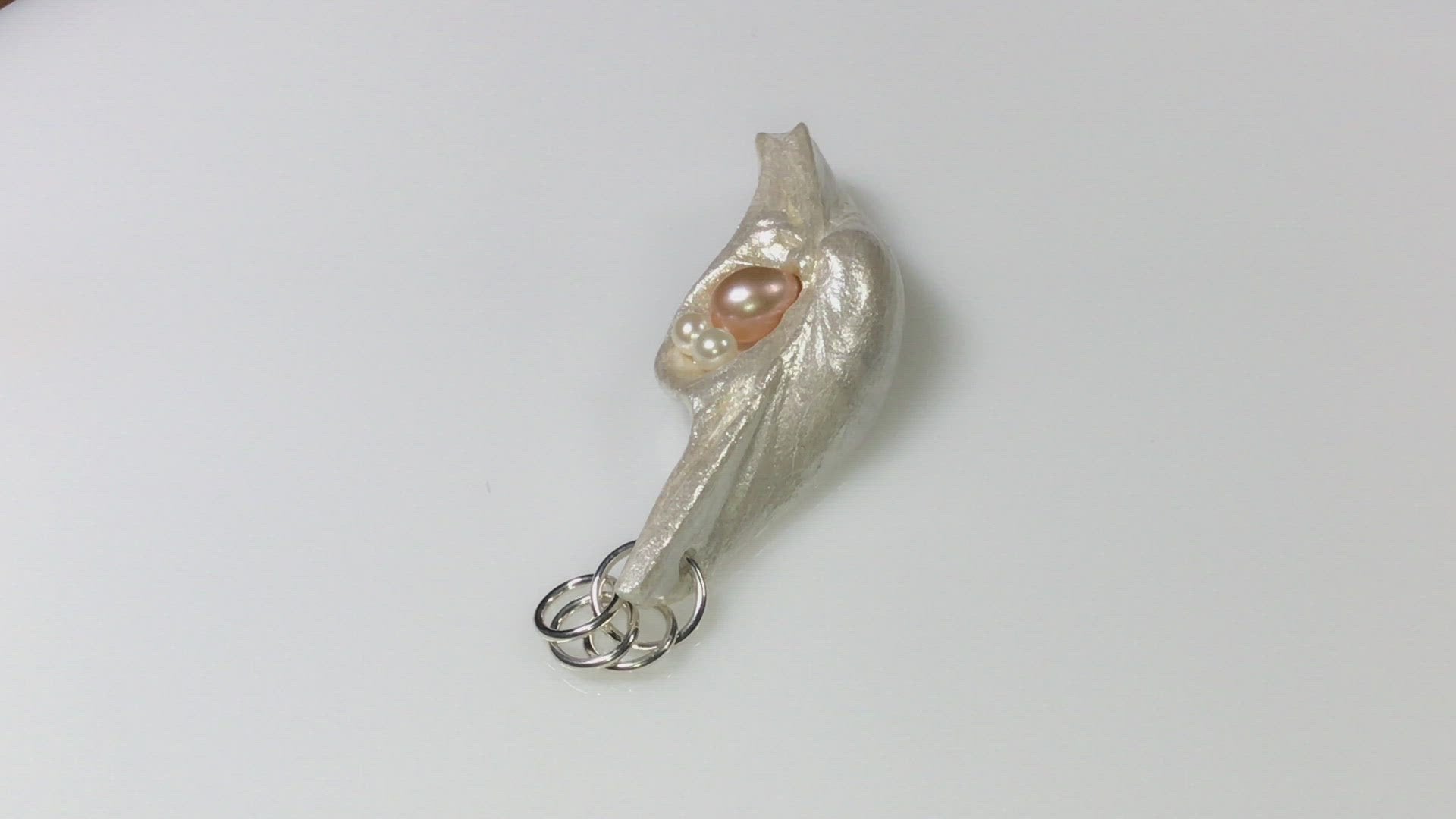 A video showcasing This natural seashell pendant has a real 7-8mm pink freshwater pearl and two baby pearls.